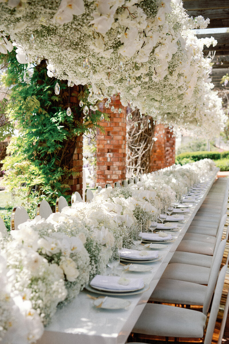 A long event table adorned with white flowers and place settings for a wedding
