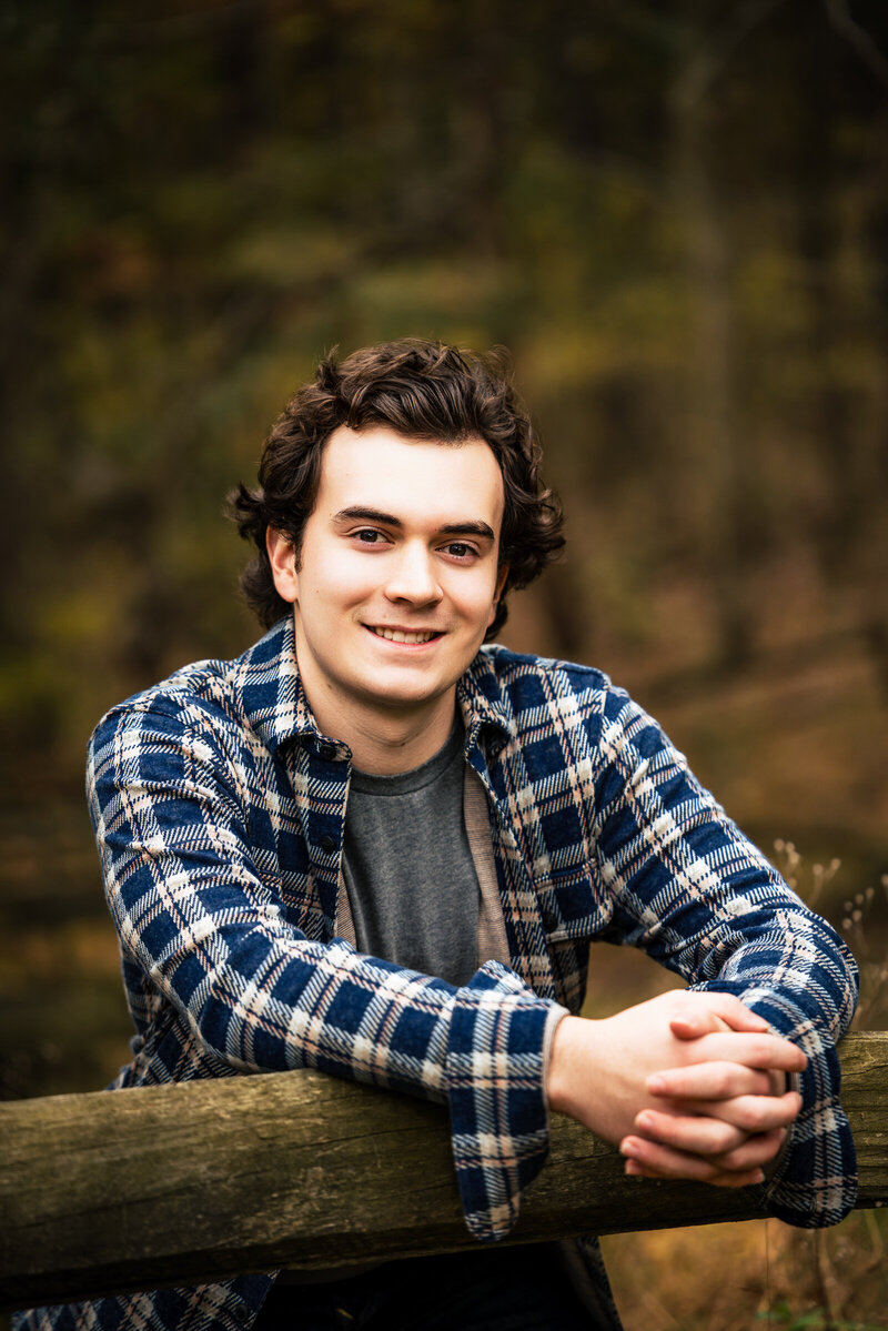 This photo of a High school graduate posing on a split rail fence wearing a flannel shirt for his senior portrait