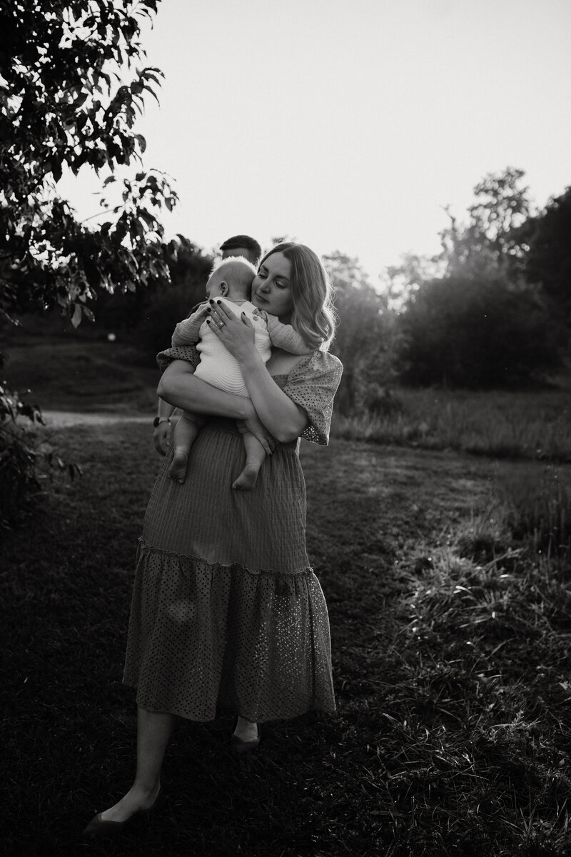 Mother carrying her baby in her arms while walking outdoors during a documentary-style motherhood photo session