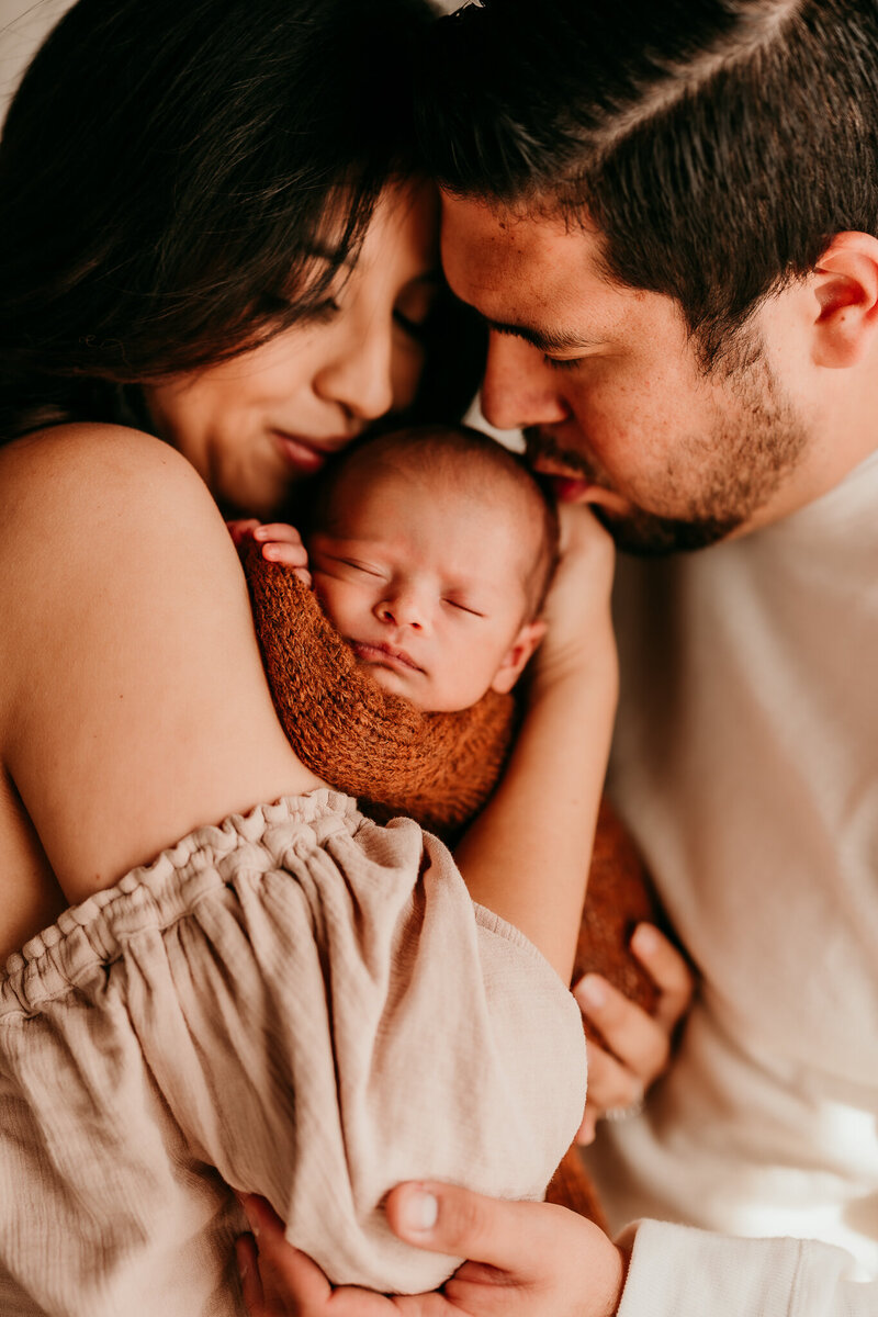 Newborn baby snuggled in parents' arms during lifestyle newborn session at Divine Light Studios in Corona, CA