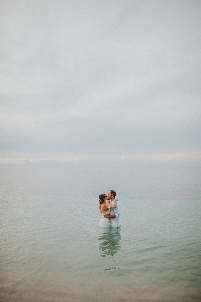 bride and groom standing in lake kissing