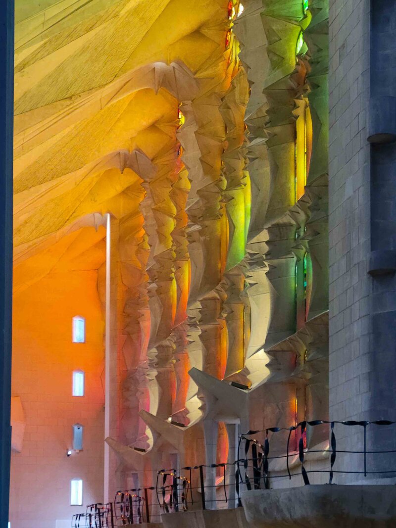 Golden and green stained-glass light filtering through the sculpted stone columns inside the Sagrada Família ©Stephanie Dosch | theViatrix Barcelona Luxury Travel Guide