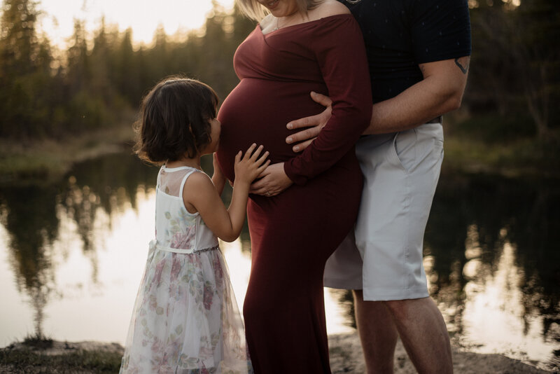 Pregnant woman in red dress with her child kissing her tummy