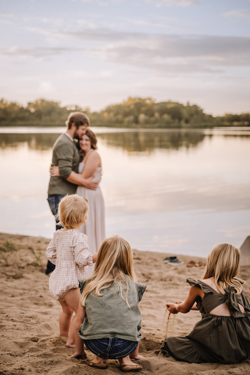 A mom and dad watching their kids play on a beach under an Iowa sunset. 