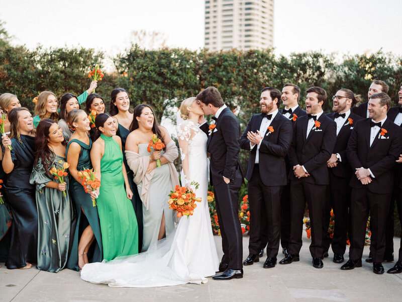 Bride and groom kissing while bridal party cheers around them