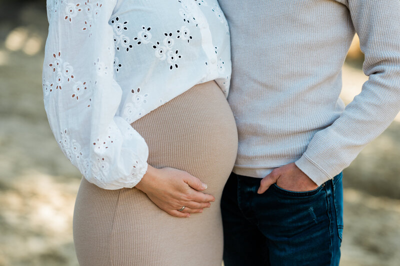 Een close-up van een zwangere buik, vastgehouden door de partner tijdens een zwangerschapsfotoshoot, vastgelegd door Monica Stout Fotografie in Dordrecht.