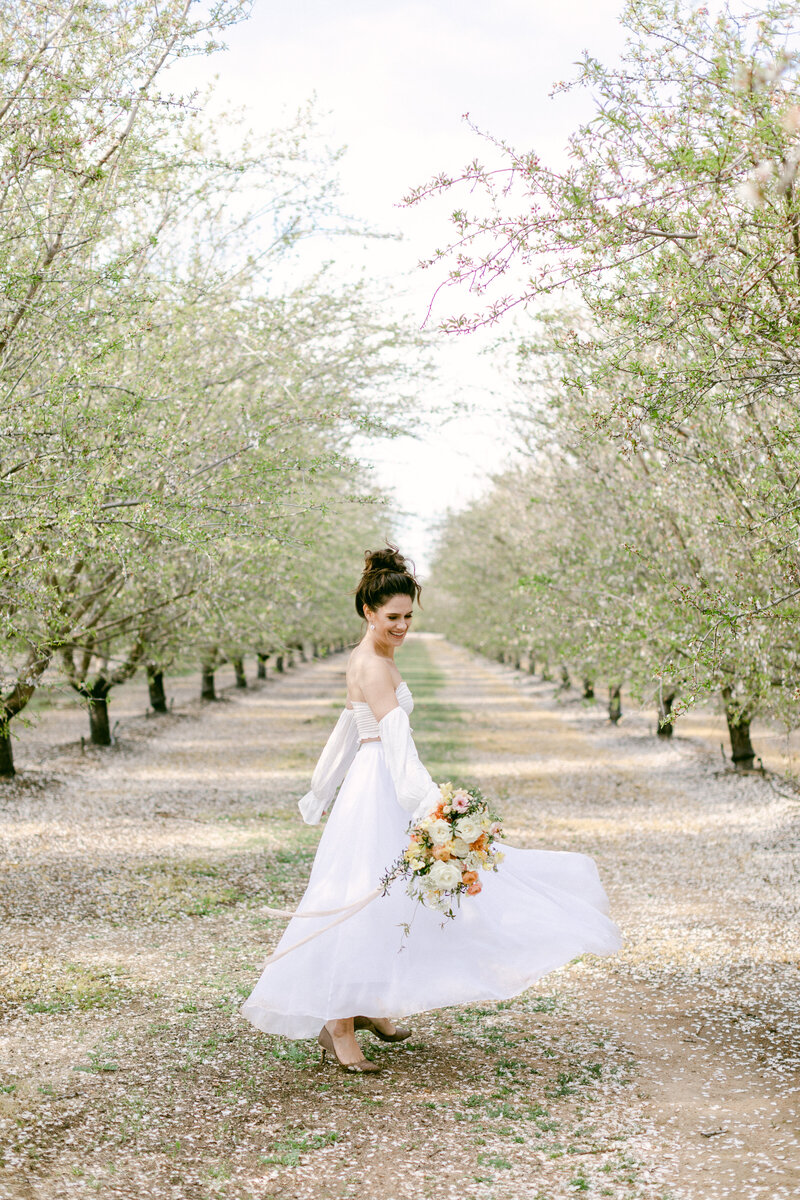 Bride spins in a row of cherry blossoms while holding her wedding bouquet