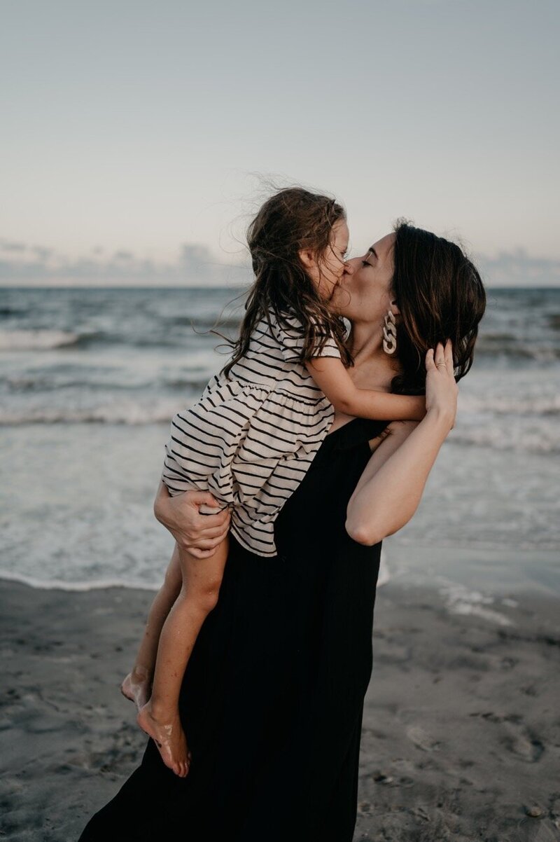 Mom and daughter kissing at a moody beach session