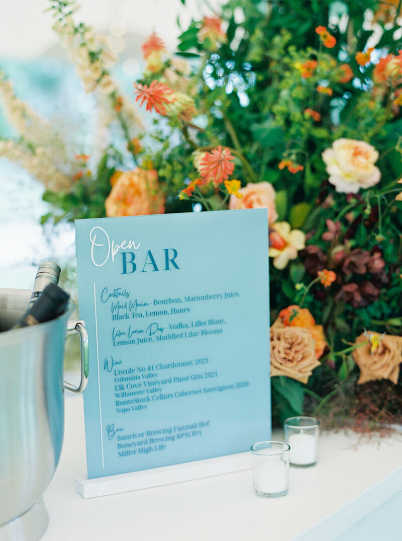Lush floral arrangement on the bar featuring peonies, ranunculus, garden roses, firesticks, foxglove, orchids, and seasonal blooms in coral, peach, and blush tones at Kelly and Joe’s wedding, designed by Summer Robbins Flowers in Bend, Oregon