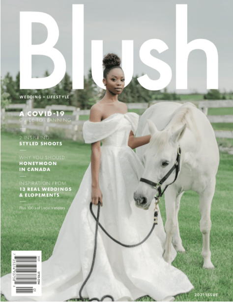 A woman in a white off-shoulder gown stands outdoors, holding the reins of a white horse on the cover of Blush magazine's 2021 issue, which focuses on weddings and lifestyle. The issue features insights from top Banff wedding planners for those seeking partial wedding planning or full service wedding planner expertise.