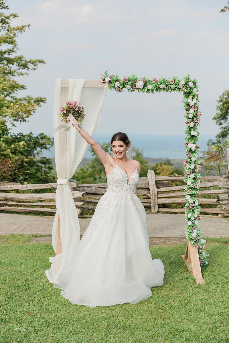 Bride standing in front of aisle holding up bouquet smiling