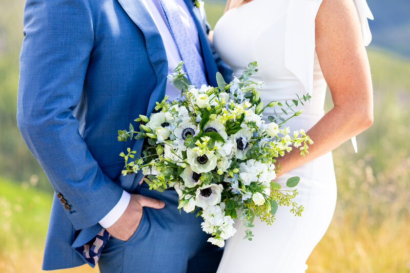 groom in blue suit and bride in her wedding dress hold bouquet of blue and white flowers