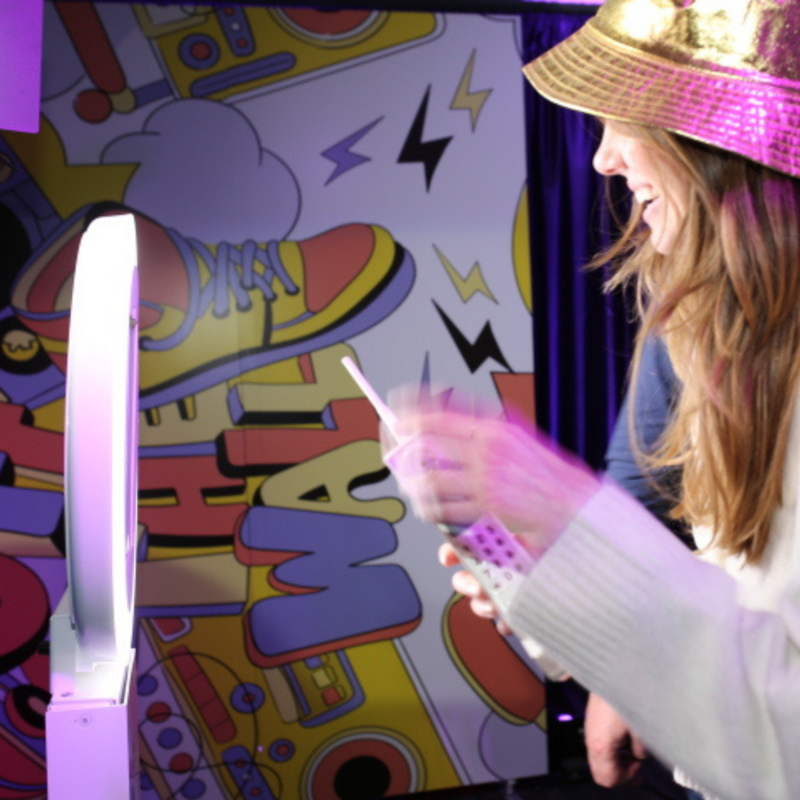 Smiling guest using MISGIF’s interactive photo booth with fun 90s-themed backdrop at a corporate event in Phoenix, Arizona, wearing a sparkly hat and holding photo props
