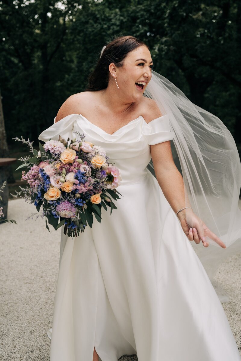 bride in paperswan bride dress laughs as her veil floats