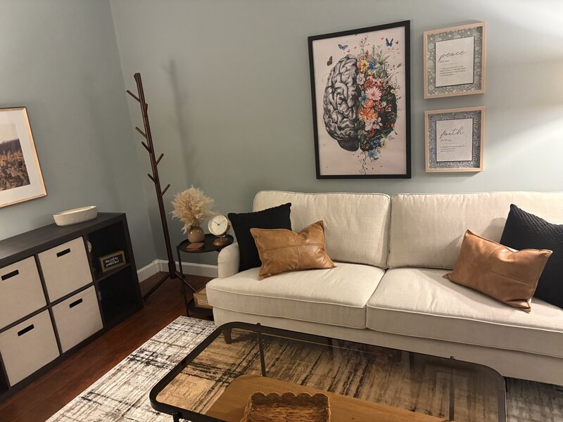 Therapy office with sofa, pillows, and brain artwork on the wall, creating a supportive environment.