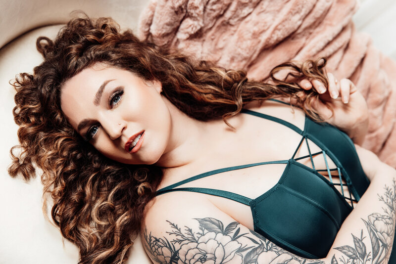boudoir portrait of a white woman with curly hair laying on a white couch with a pink blanket