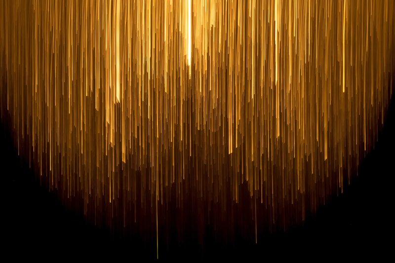 Abstract golden rays of light cascading vertically against a dark background.
