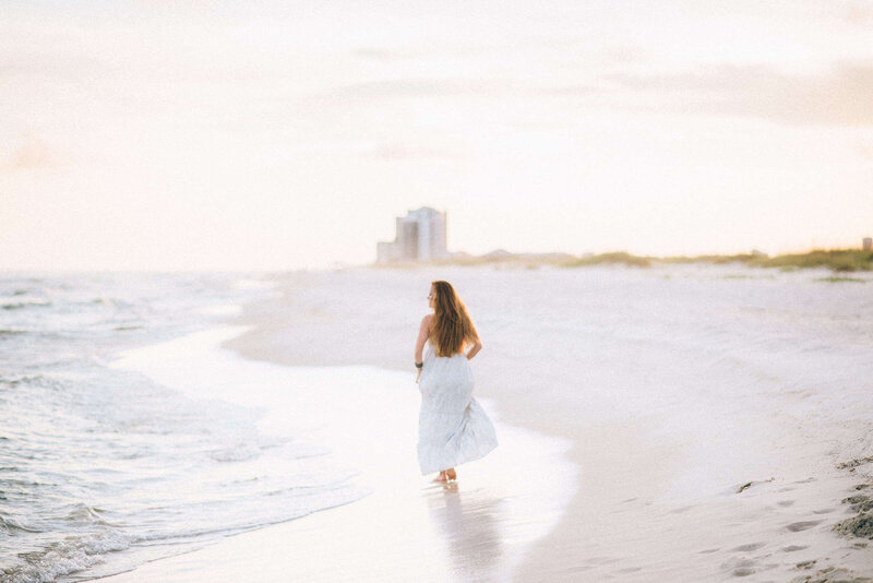 Elegant woman in white dress running on sandy beach