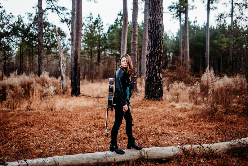 a senior girl walking on a fallen tree with her guitar on her back