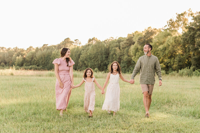 Family walks in a field holding hands during a family session in Raleigh. Photographed by Raleigh family photographers A.J. Dunlap Photography.