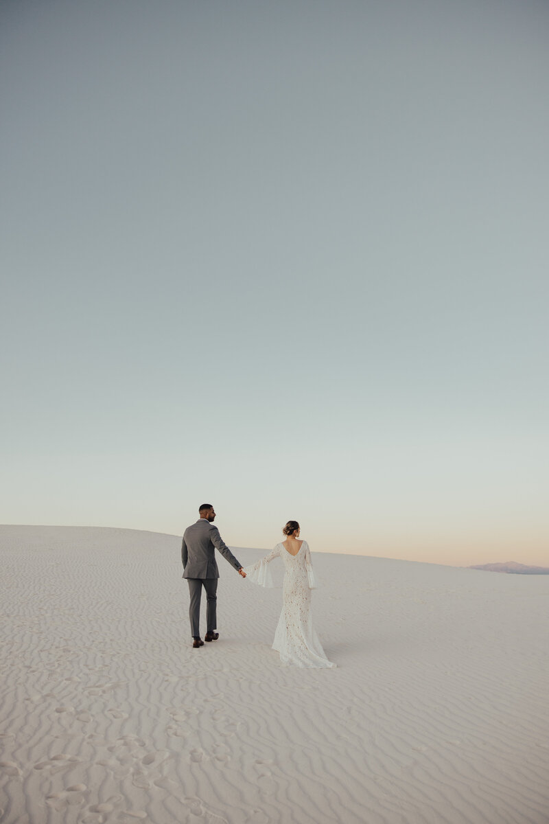 bride and groom holding hands walking on sand dune
