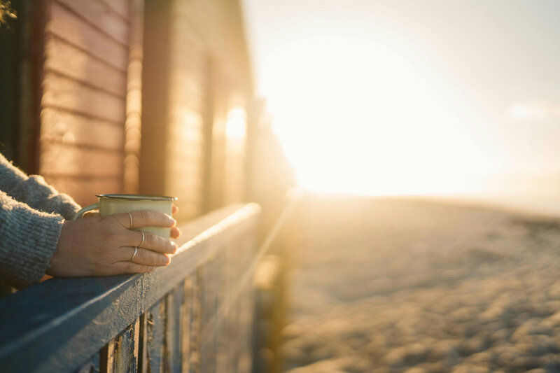 Woman holding a mug of coffee as she leans over a deck admiring the sunrise