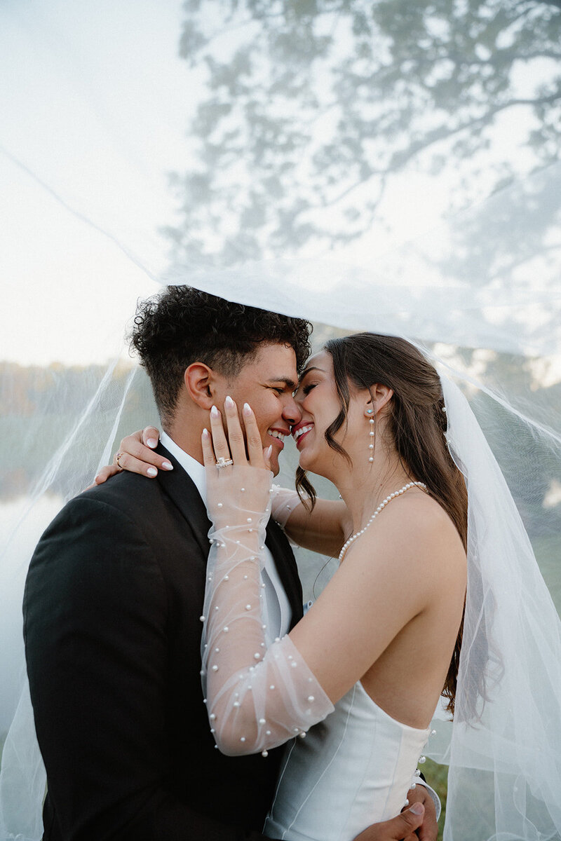 romantic and dreamy photo of bride and groom smiling at each other while under a veil