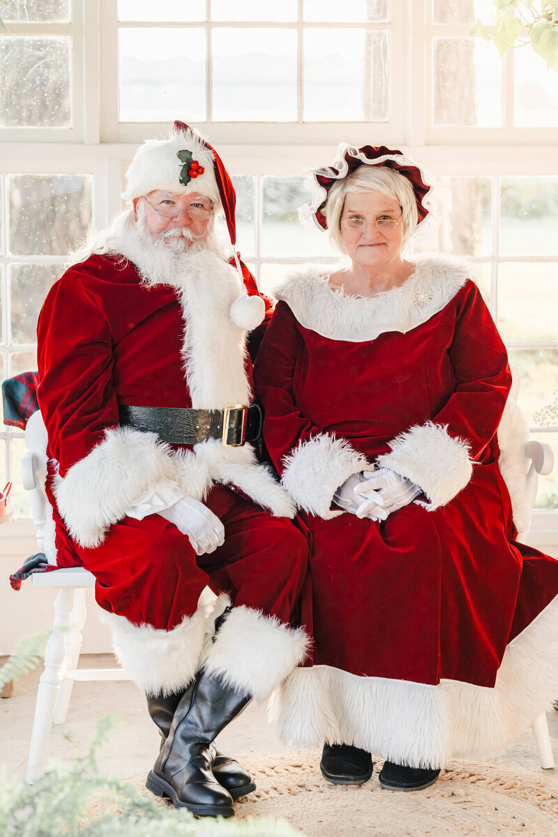 Santa and Mrs. Claus sit on a bench in a sun porch in Chesapeake, VA. They both smile for the camera.