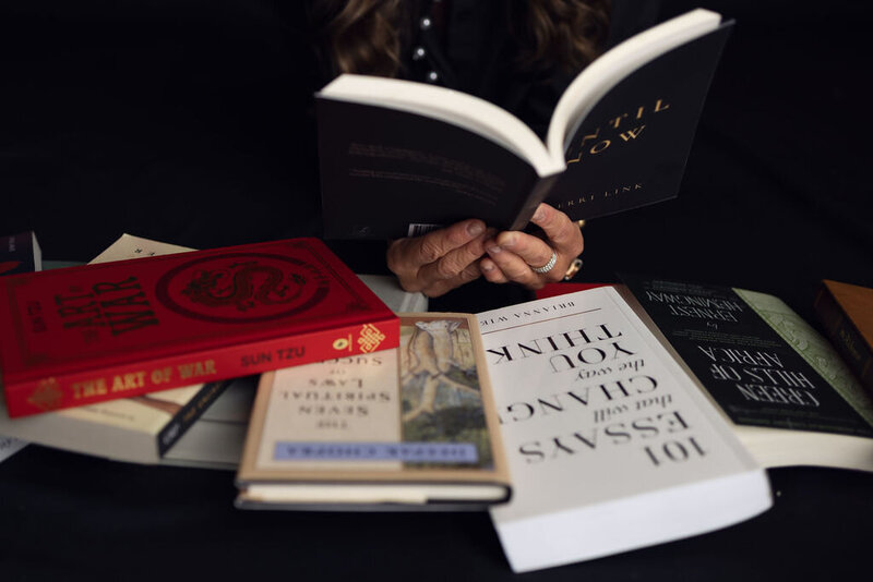 A close-up view of a woman’s hands holding an open book surrounded by titles on healing, purpose, and transformation.
