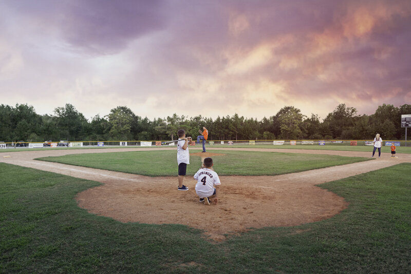 Family lifestyle portrait on a Montgomery, TX baseball field by Sarah Farmer, capturing cherished family moments.