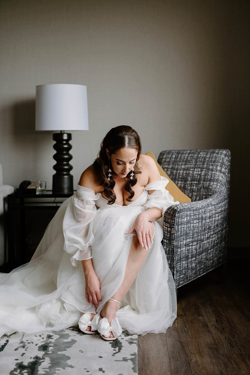 A person in a wedding dress sitting down and putting on heels 