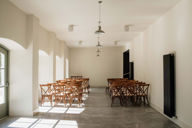 A wide photograph of a newly renovated barn space. The space is white and has concrete floors, the space is set up as a wedding venue.