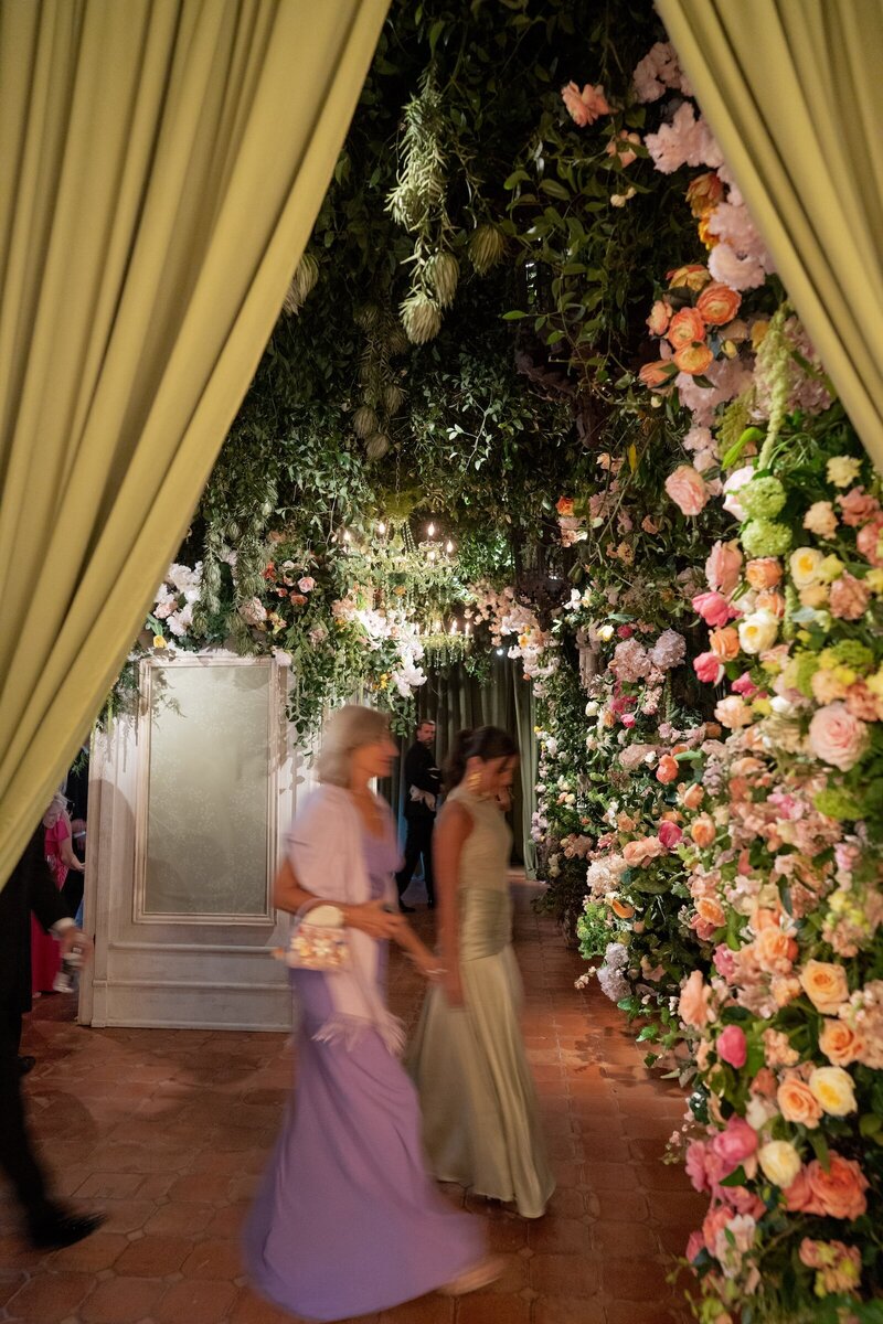 Wedding guests arriving to a wedding reception, with a colorful floral wall and light green curtains