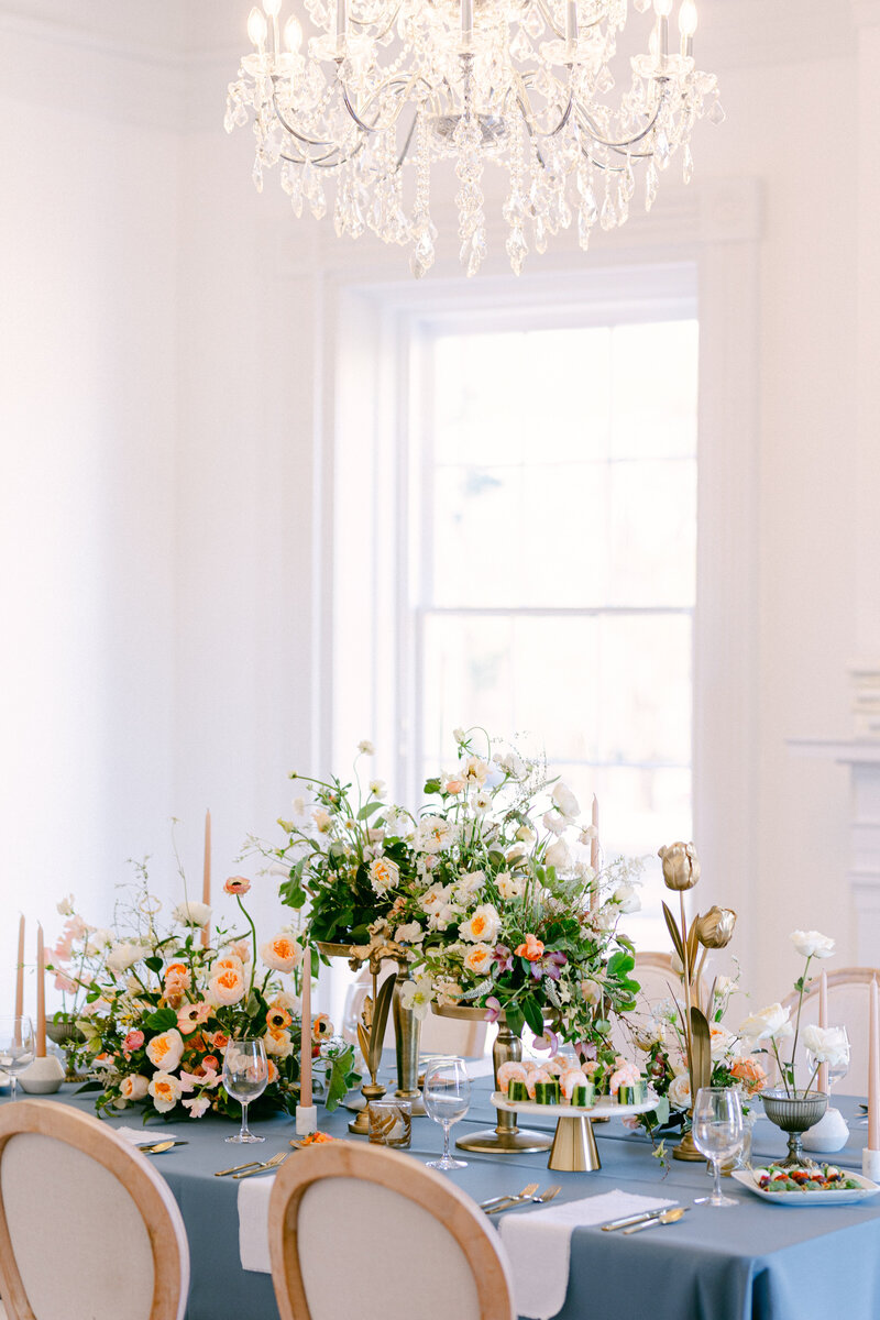Table setting with floral arrangements, blue tablecloth, chandelier.