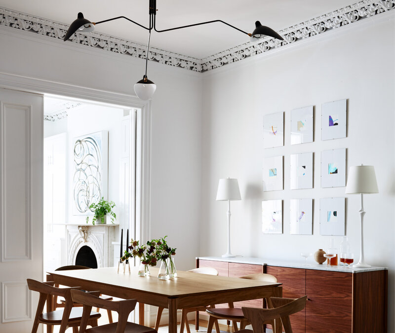 Top interior decorators in Boston created a modern dining room in a historic brownstone with an oak table, black modern lighting, and simple white walls.