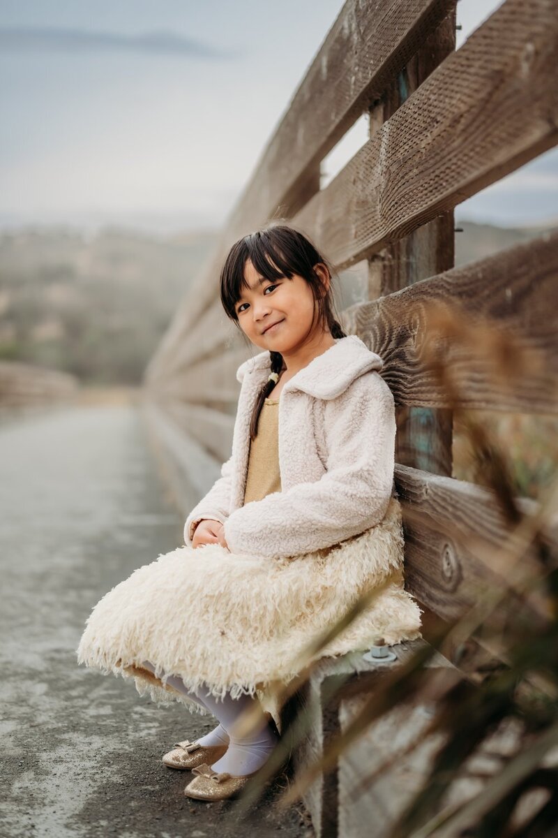 young girl sits on bridge smiling at camera