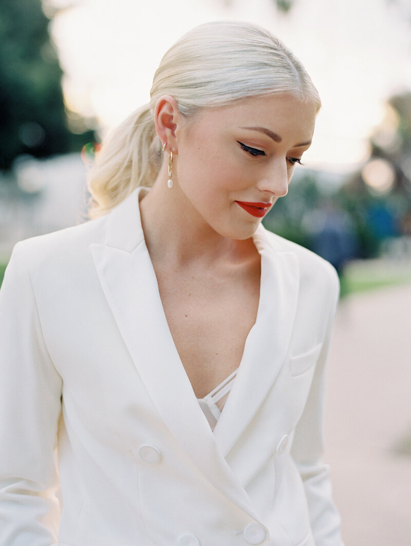 bride during engagement session wearing a white double button fitted pant suit  with red lipstick and pearl earrings
