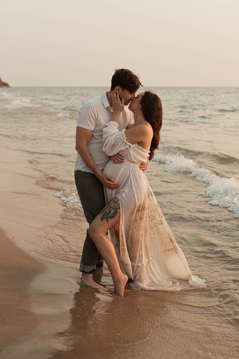 Pregnant couple embracing on shoreline at golden hour captured by Michigan maternity photographers
