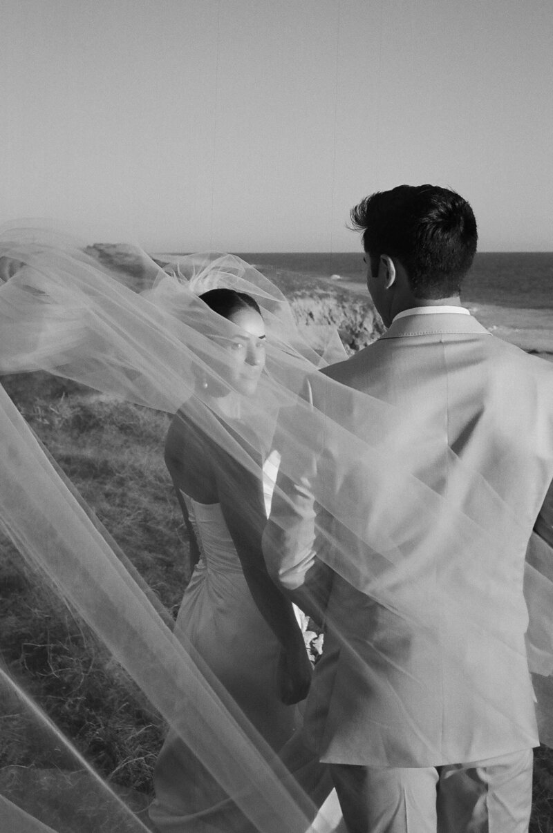 bride and groom holding hands on the cliffside next to the ocean