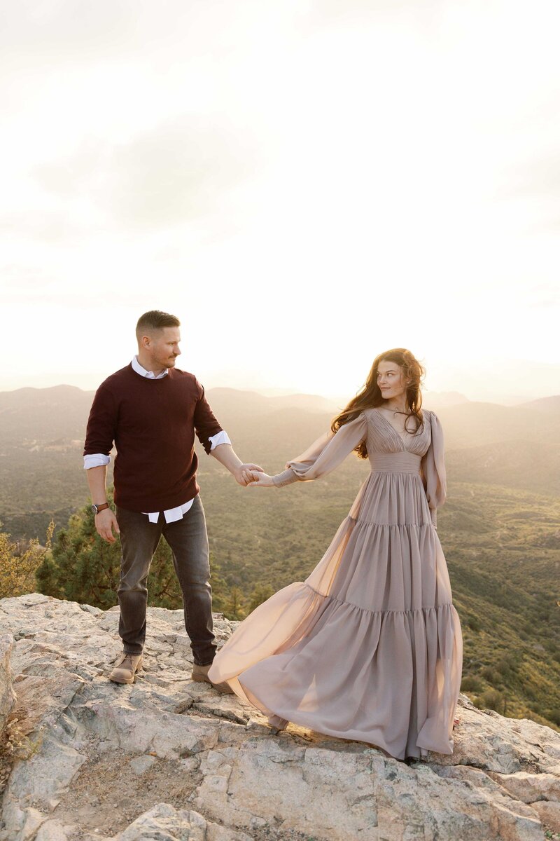 Couple walks romantically hand in hand on cliffside.