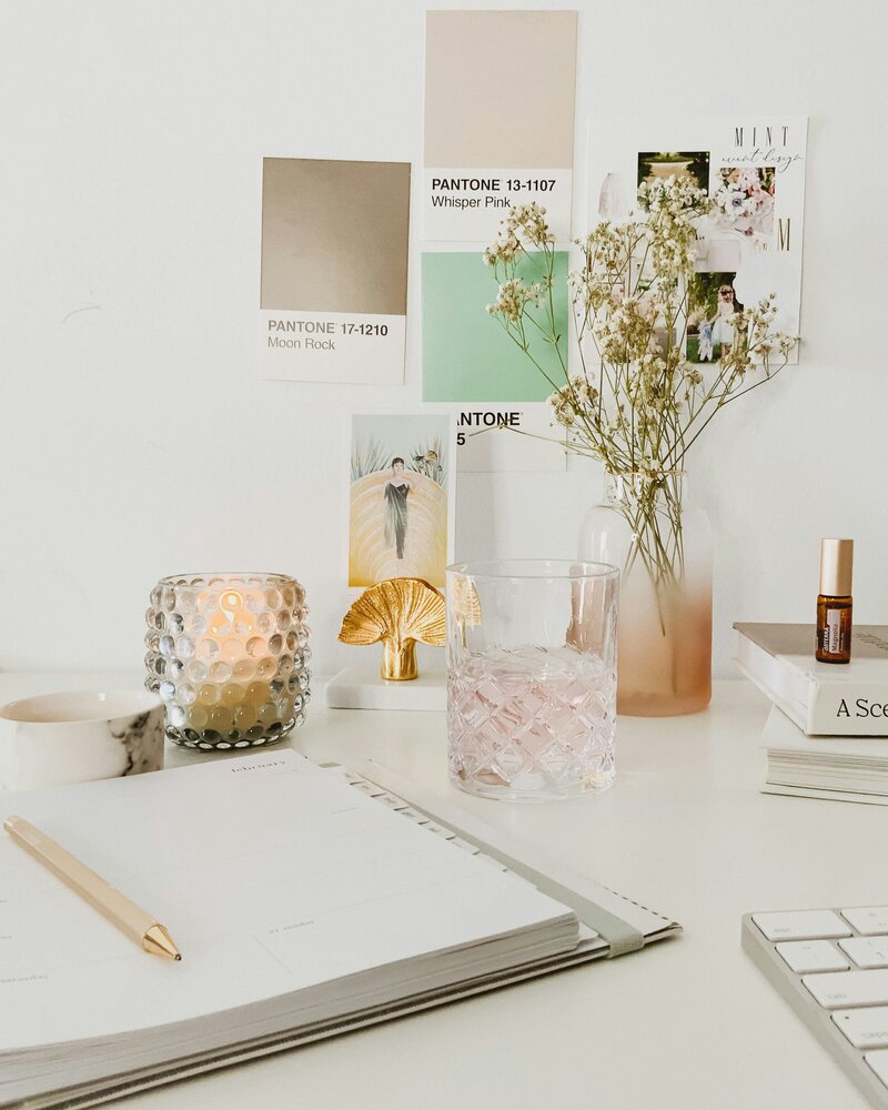 desktop with candles burning, makeup, planner, and other lifestyle items on vanity in all white photo