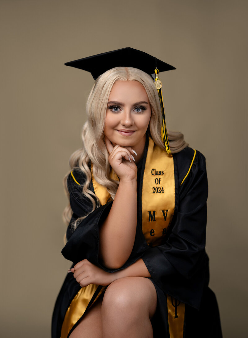 Jenni Nikki Photography took this graduation photo at her Woodstock photo studio of girl in KSU cap and gown. It is a close up headshot with her hand on chin and smiling.