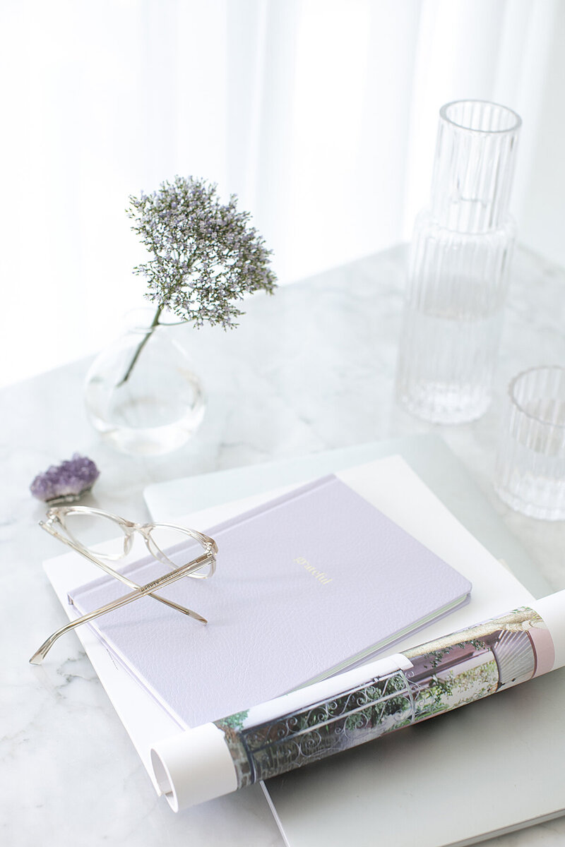 The Purple Flamingo brand strategy guide on display: with a glass of water, purple flower, and an amethyst crystal, signifying the creative and holistic approach to branding.