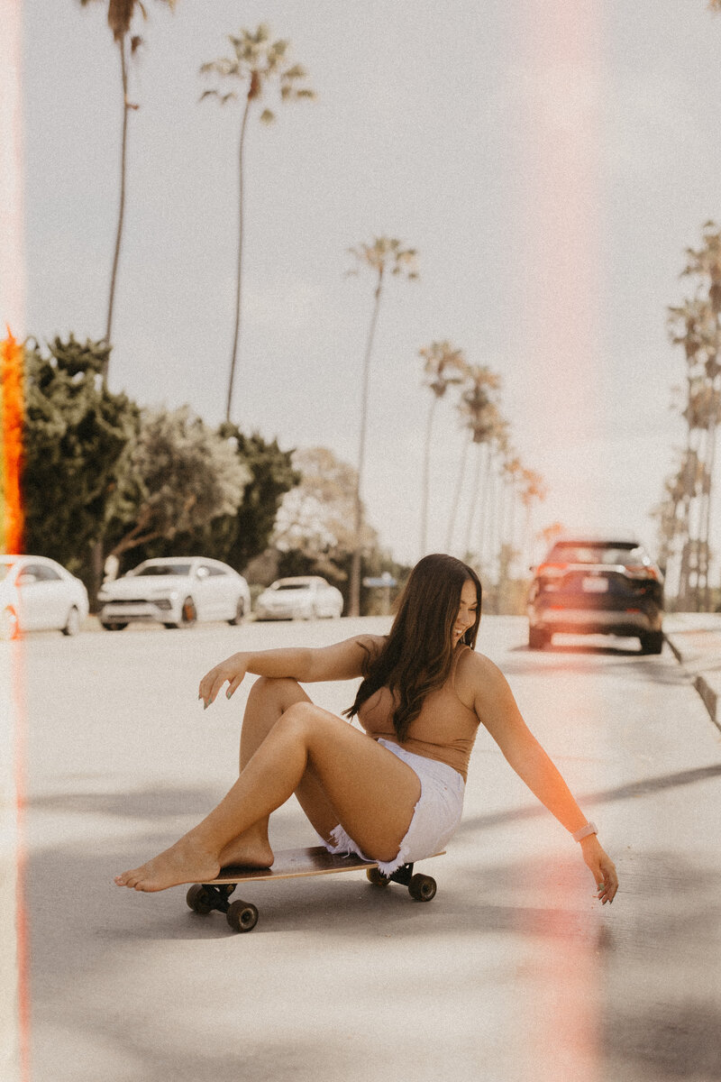 Girl smiling, sitting down on a skateboard.