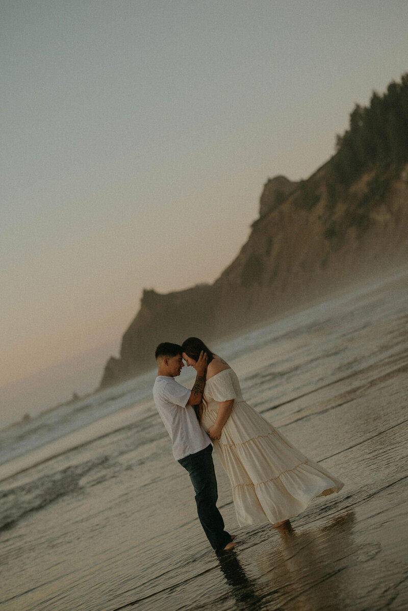 Expecting parents capturing their maternity photos during the blue hour in Lincoln City, Oregon, with the ocean as a serene backdrop.