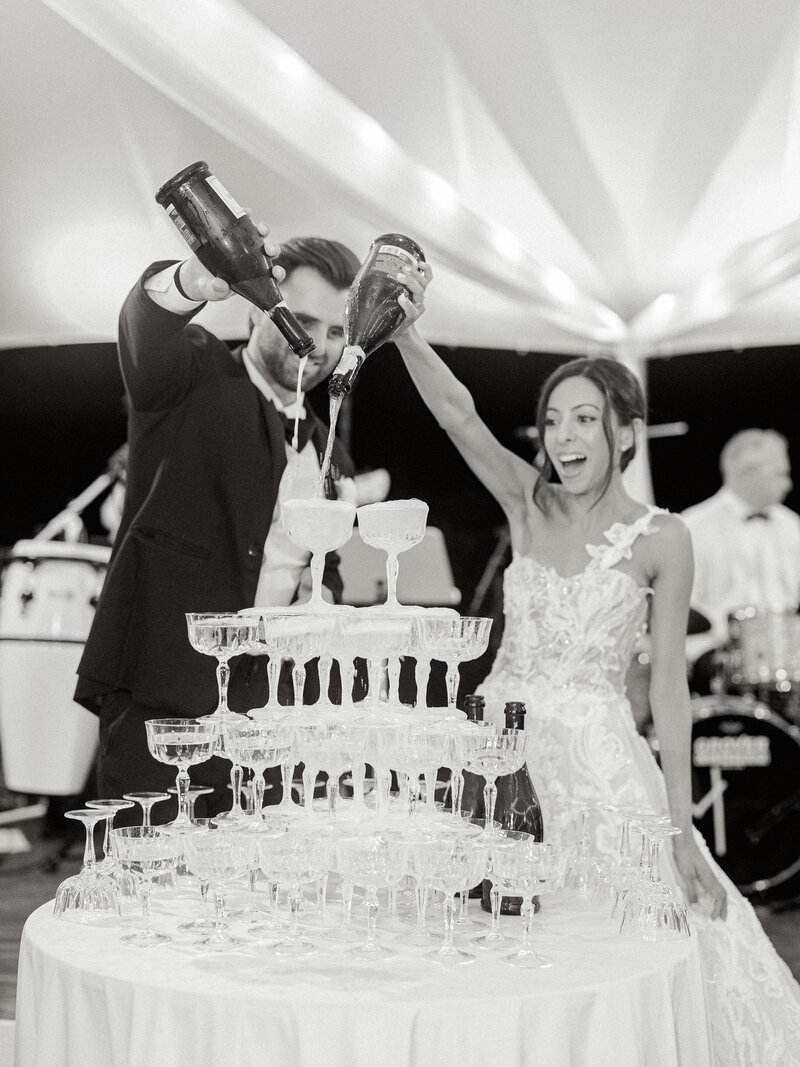 Black and white photo of the couple pouring champagne into their champagne tower.