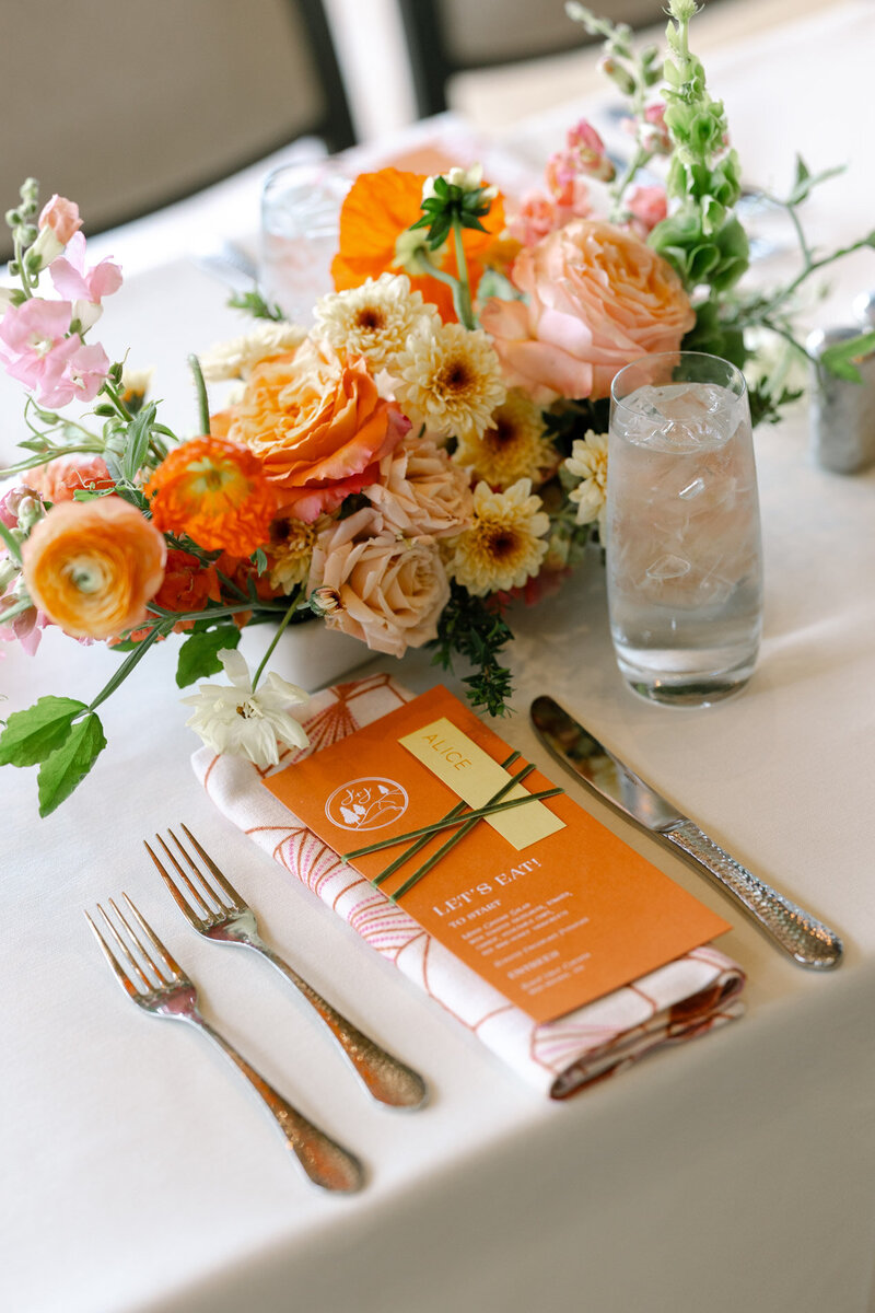 Coral wedding menu on a printed napkin featuring florals, patterned napkins and calligraphy details representing full service design and calligraphy by Life in Letters.