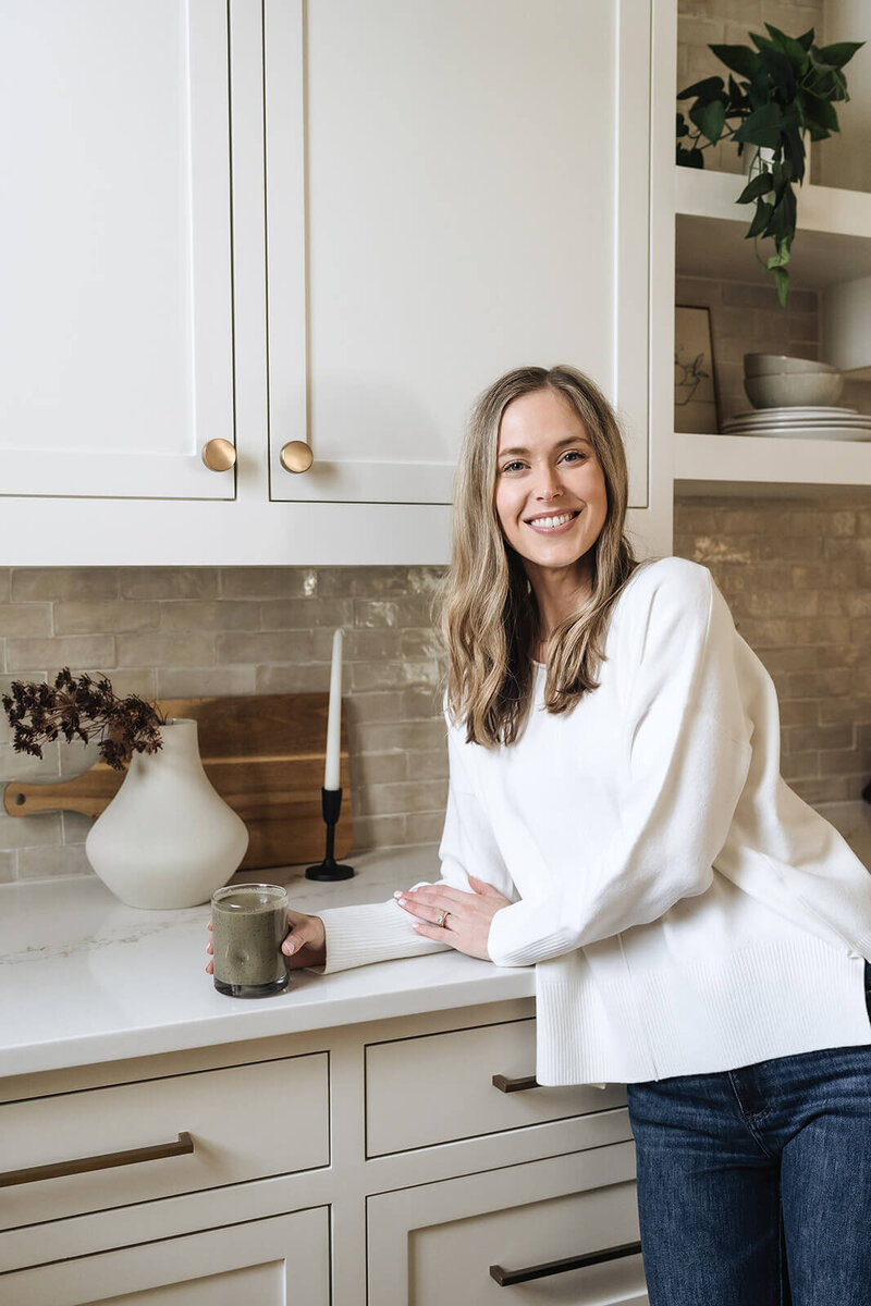 Health and wellness coach for moms in early motherhood enjoying a nutrient-packed green smoothie in a bright kitchen, promoting simple real-life nutrition habits