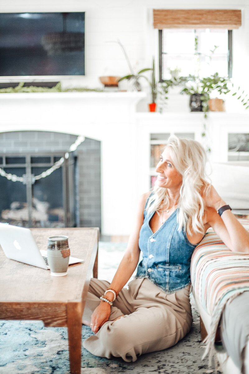 Relocation real estate agent Stephanie sits on the floor in her living room and leans against a couch.