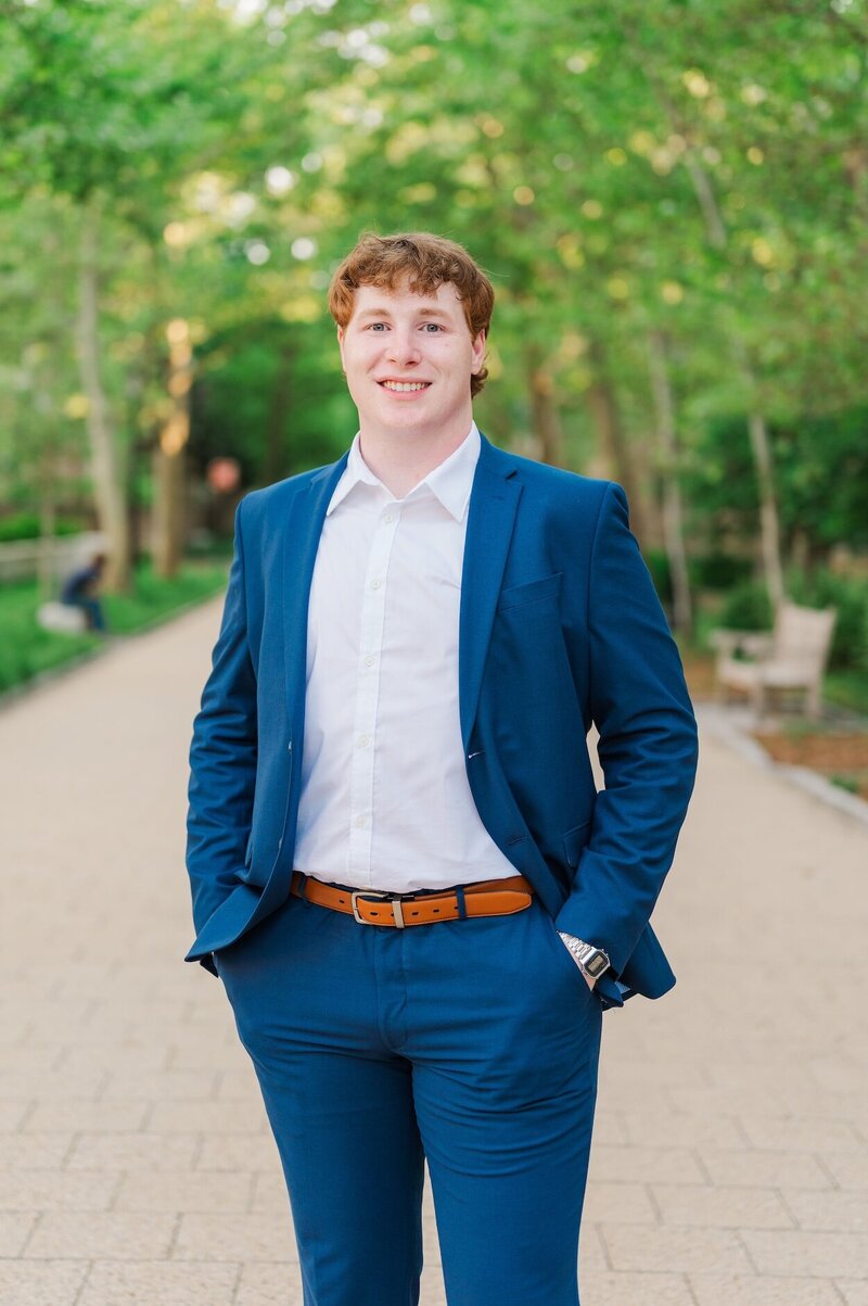 A Yale University senior wearing a blue suit smiles with his hands in his pockets.